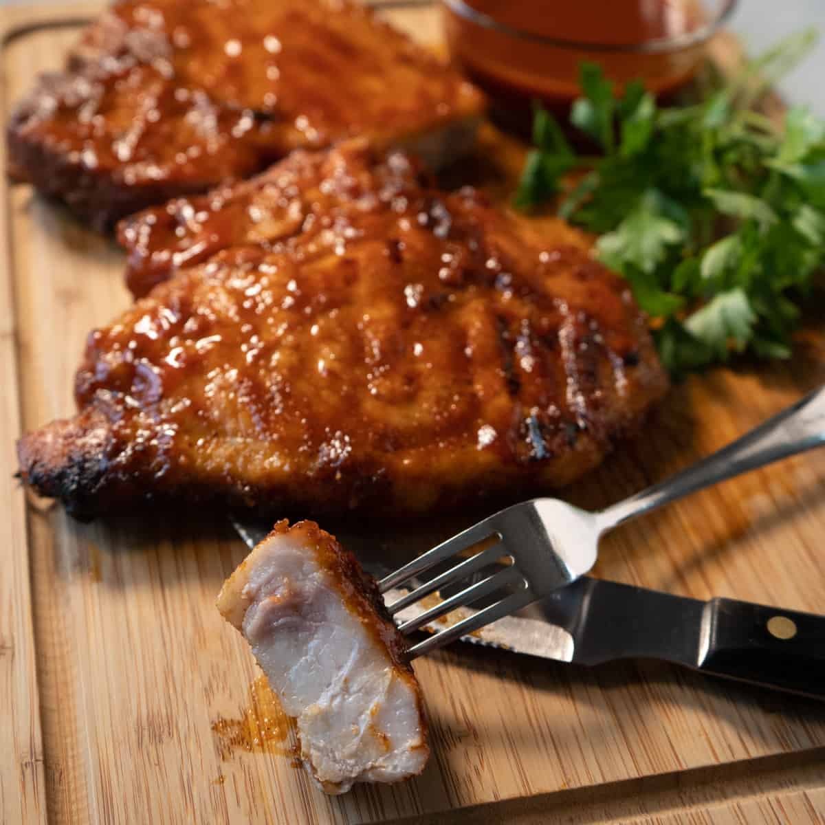 cooked pork chops on a board with a bite size piece on a fork.
