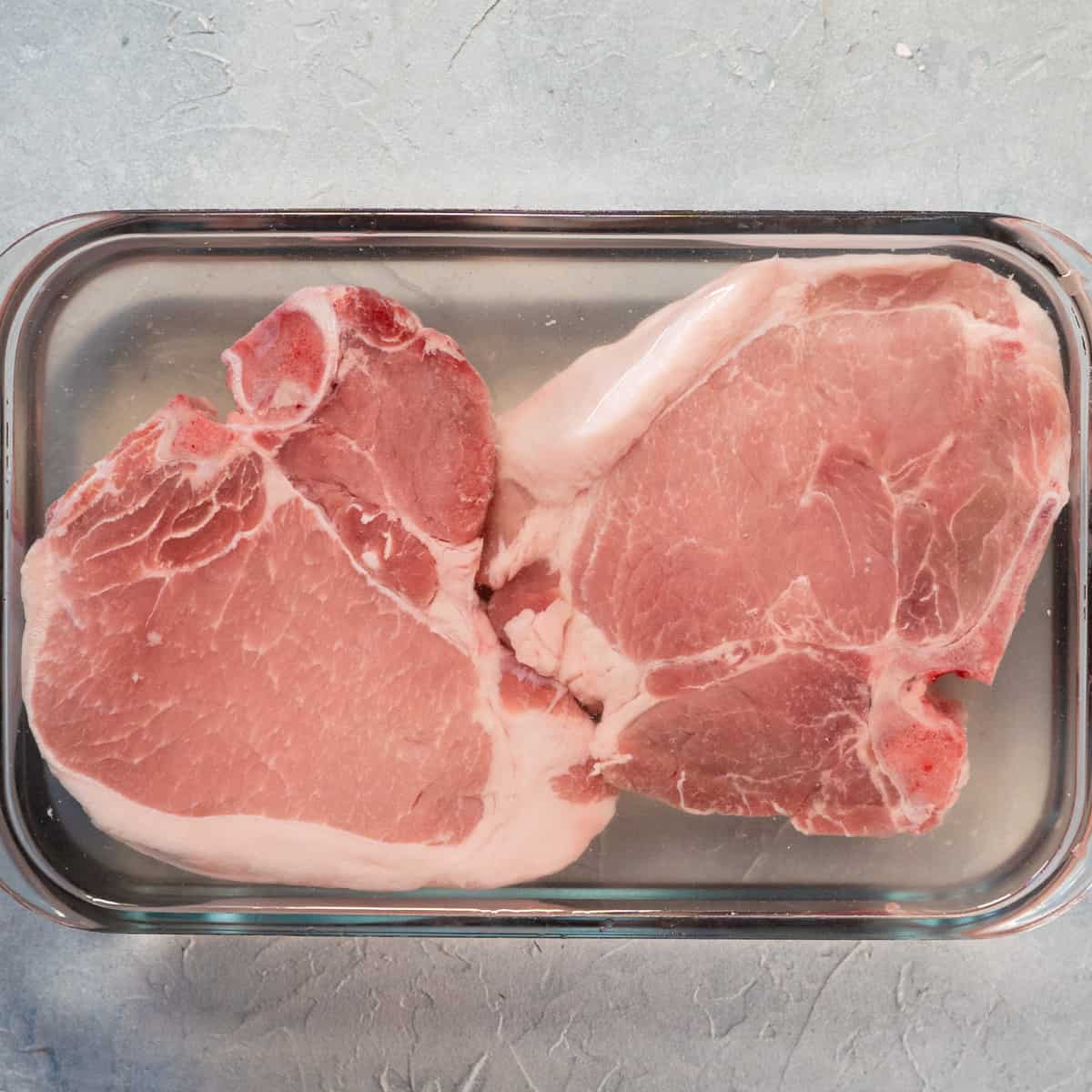 pork chops submerged in brining liquid in a glass dish.