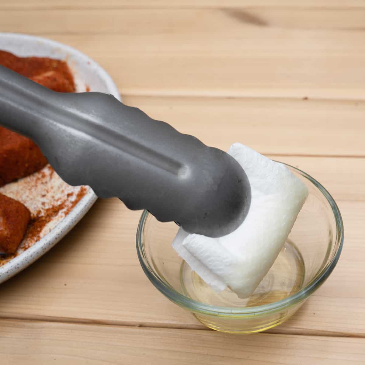 Tongs holding folded up paper towel dipped in oil.