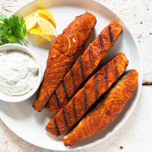 grilled salmon fillets on a white plate with a side of sauce.