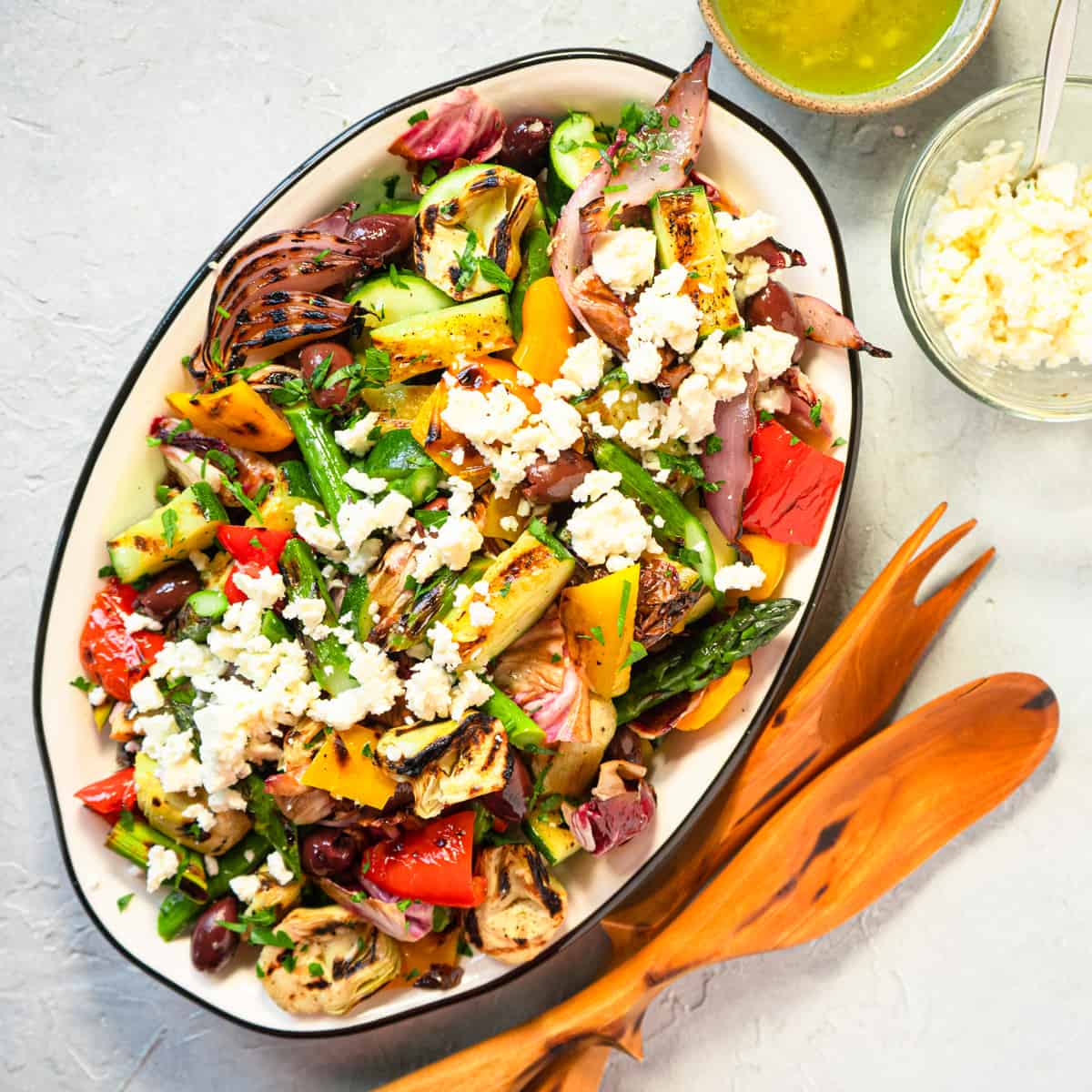 grilled vegetable salad on an oval platter with feta cheese and extra vinaigrette on the side.