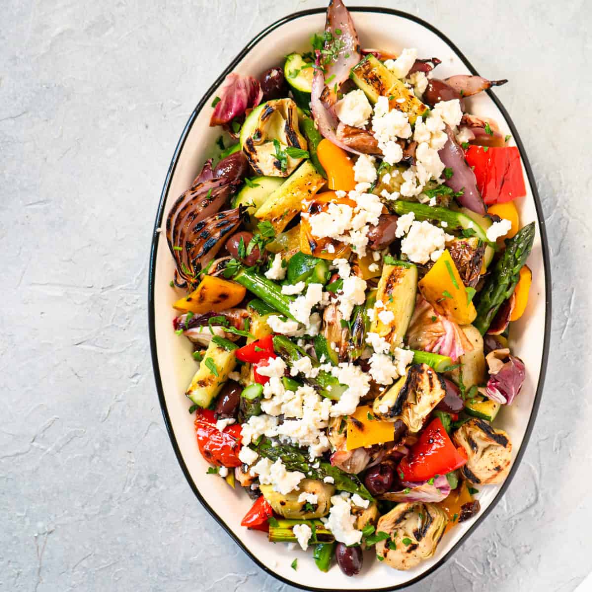 Mediterranean grilled vegetable salad on an oval dish garnished with feta cheese and Kalamata olives.