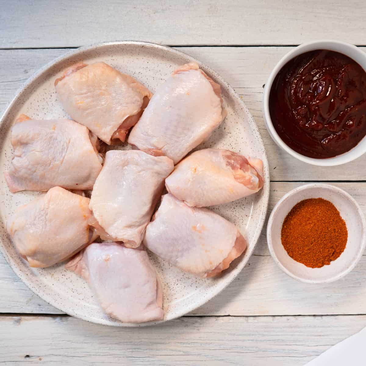 Raw chicken thighs, spice rub and bbq sauce on a white background. 