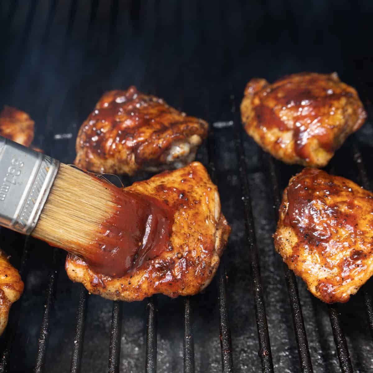 Brushing BBQ sauce on the chicken while on the grill. 