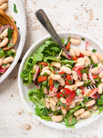 One serving of white bean salad on a bed of arugula with a fork.