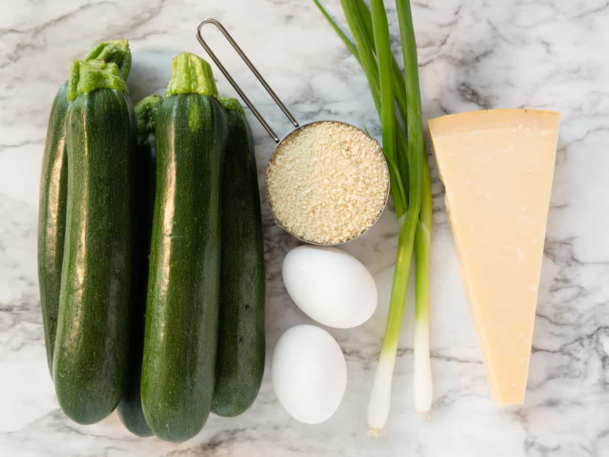 Ingredients to make zucchini fritters on a marble surface.