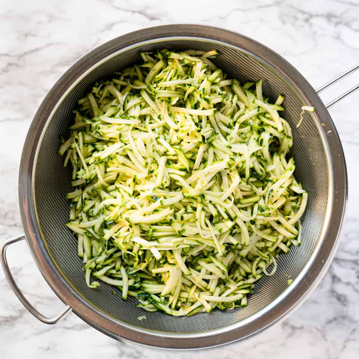 Shredded zucchini resting in a sieve sprinkled with salt.