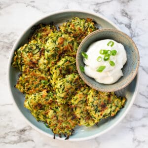 Baked zucchini fritters on a plate with a side of sour cream garnished with sliced green onions..