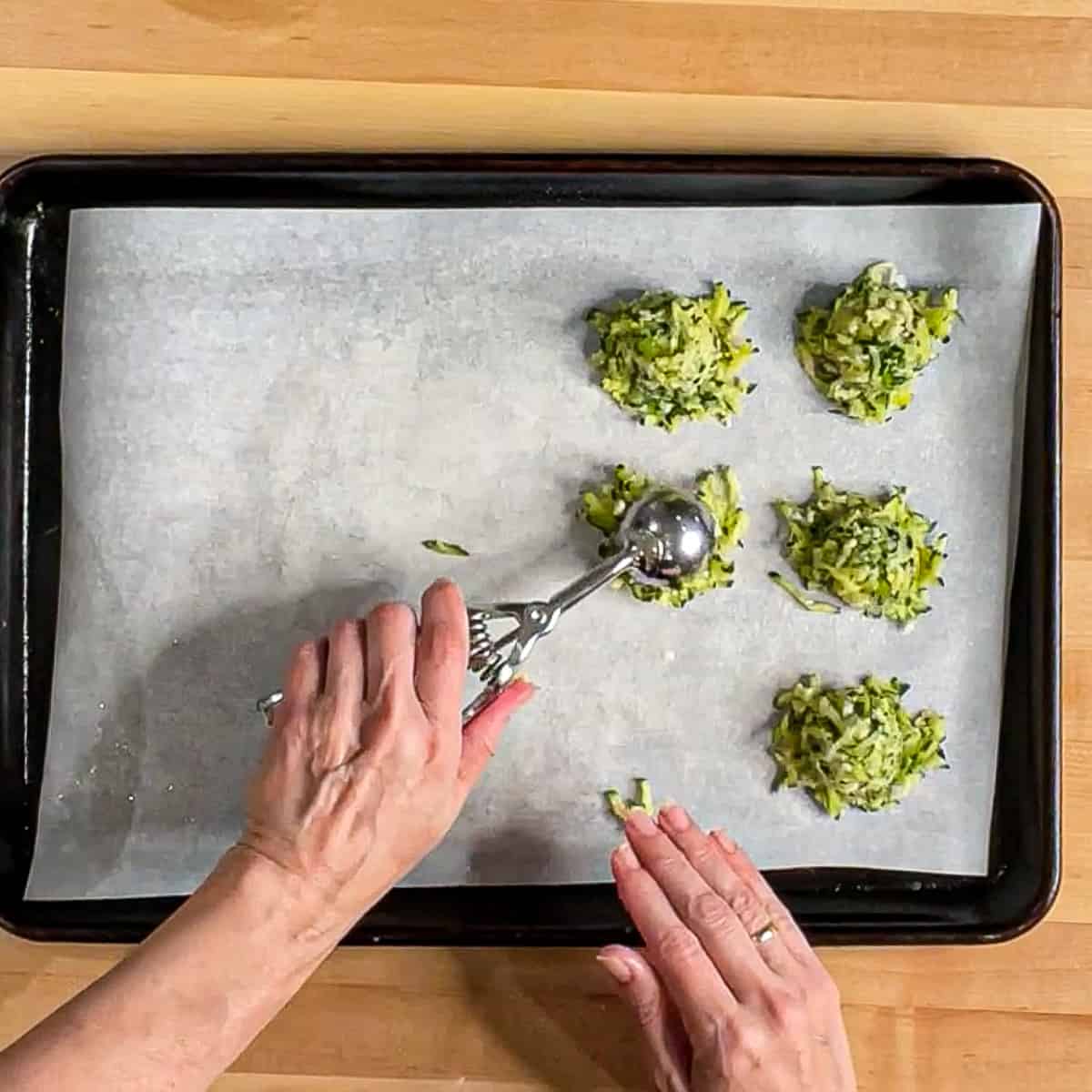 Scooping zucchini fritter batter onto a tray.