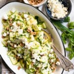 shaved zucchini salad on an oval plate with walnuts and feta on the side.
