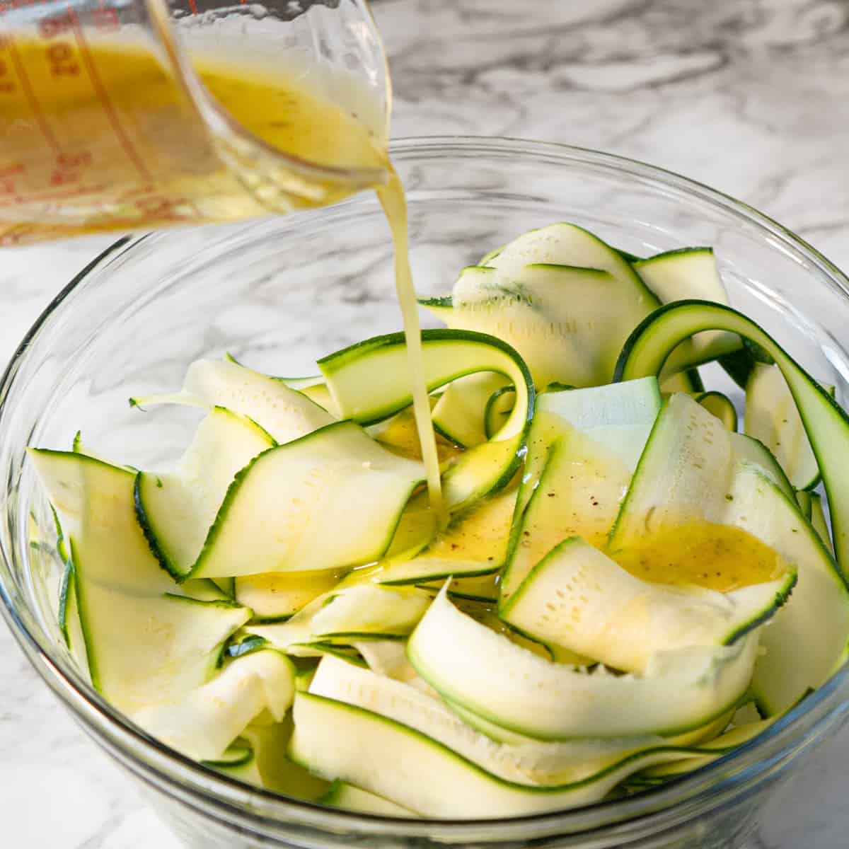 dressing being poured over shaved zucchini.