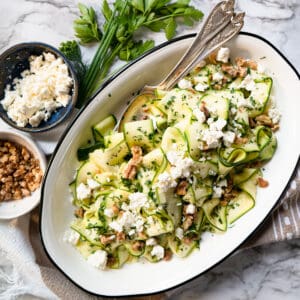 shaved zucchini salad on an oval plate with walnuts and feta on the side.