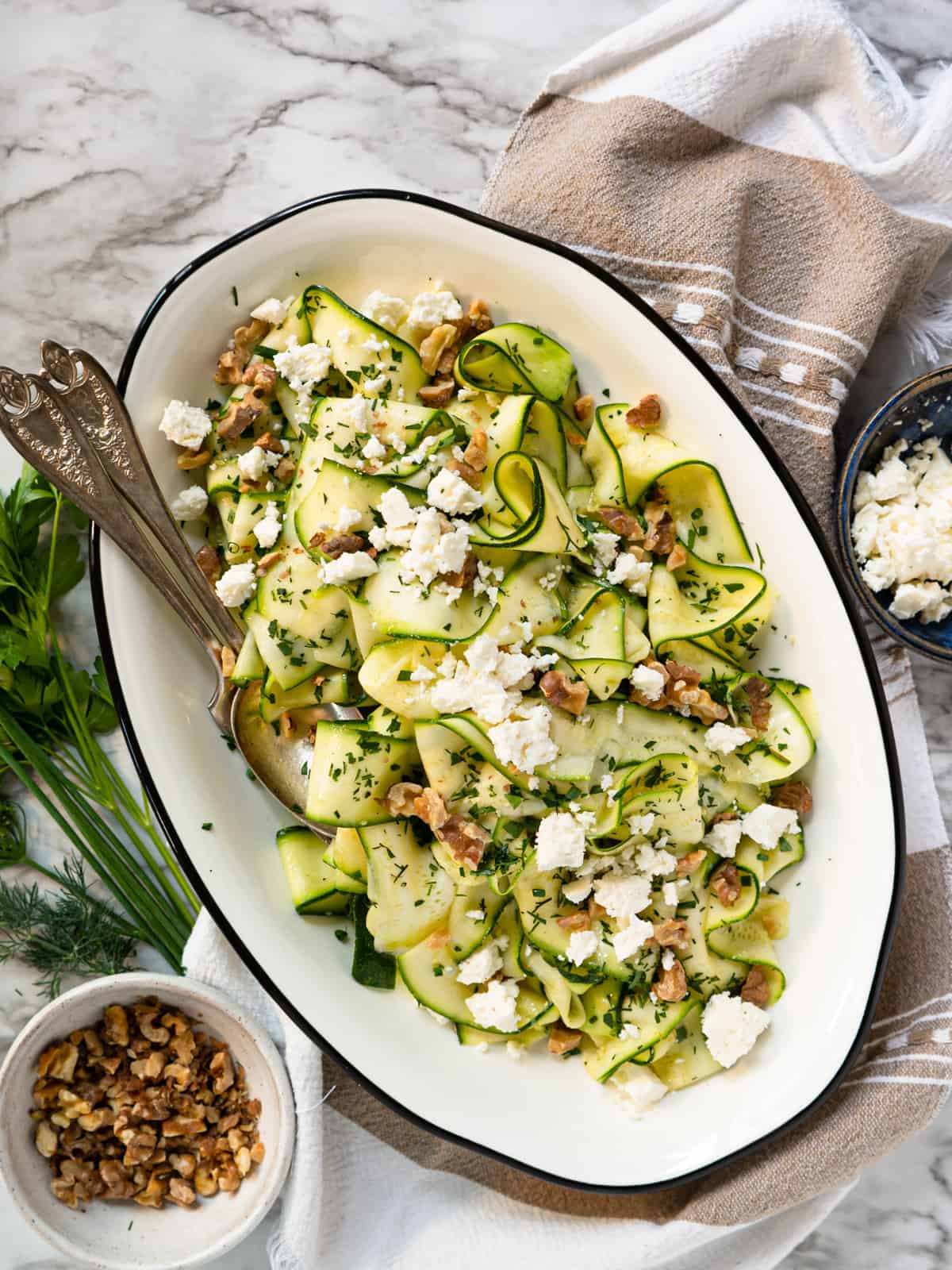 shaved zucchini salad on an oval plate with walnuts and feta on the side.