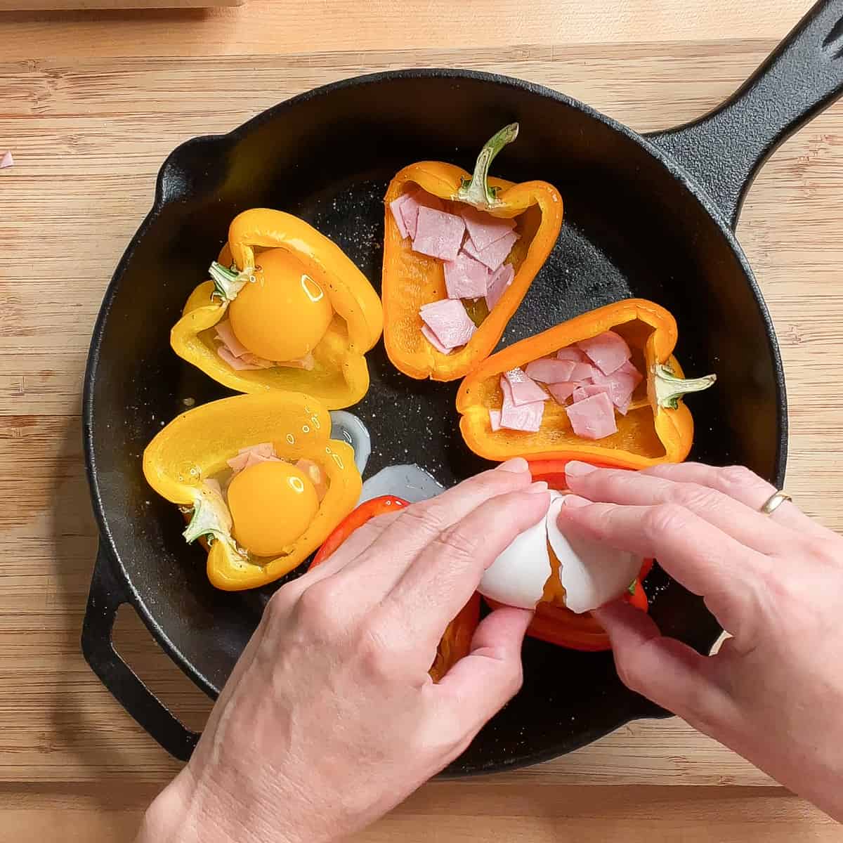 eggs being added to the pepper cups on top of chopped ham.