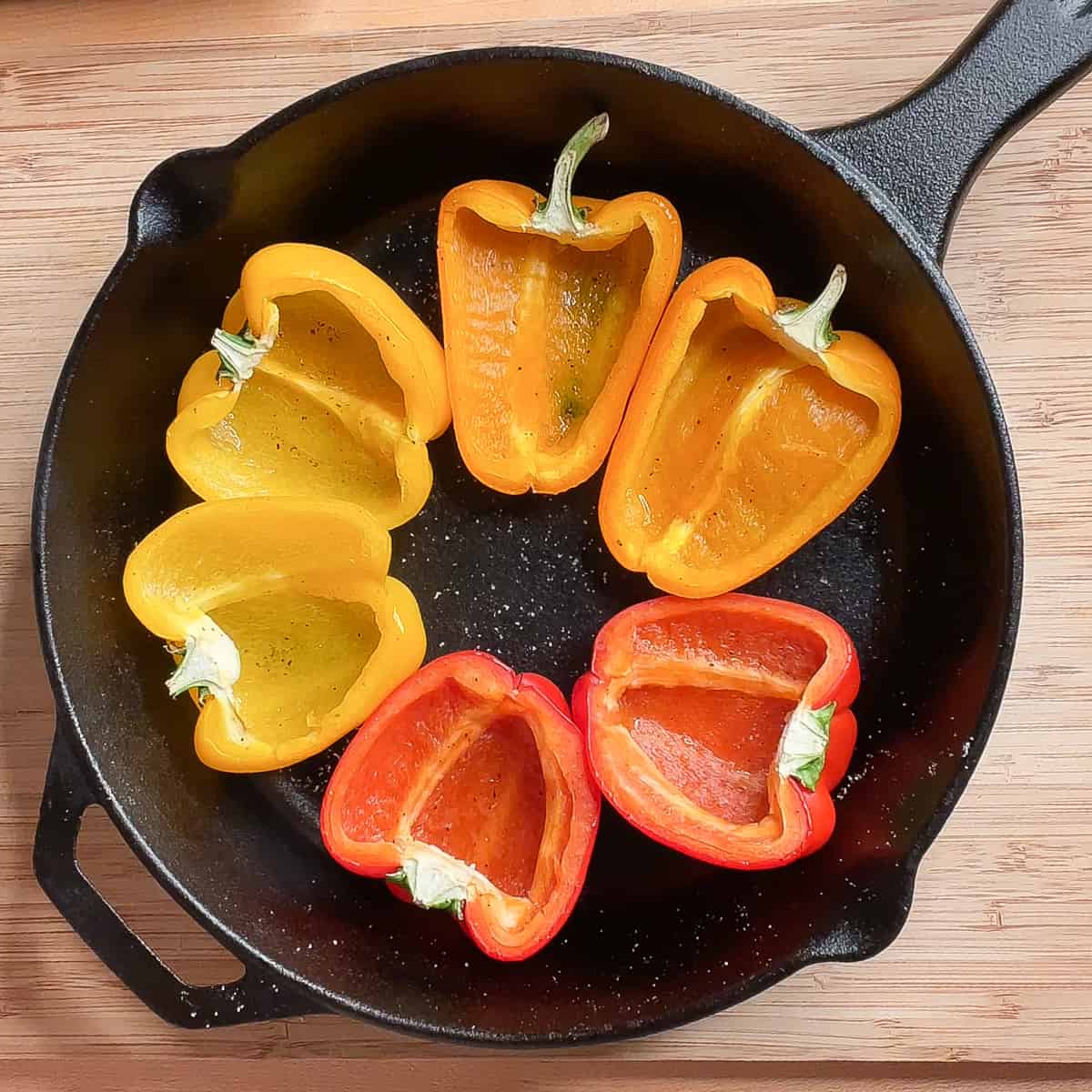 6 pepper halves sitting cut side up in a cast iron skillet.