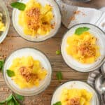 4 small glasses of coconut panna cotta topped with chopped mango and toasted coconut.