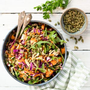 easy fall salad in a blue ceramic bowl with a side dish of toasted pumpkin seeds.