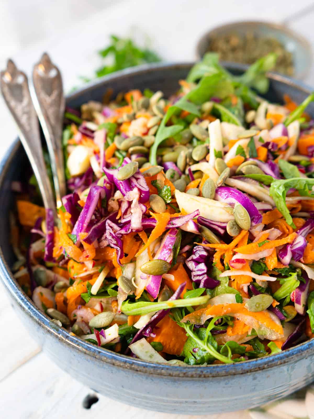 colorful fall salad in a blue ceramic dish with serving spoons.