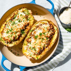 finished stuffed spaghetti squash garnished with fresh parsley in a casserole dish with Parmesan cheese on the side.