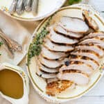 sliced turkey breasts on a china platter with gravy boat on the side.
