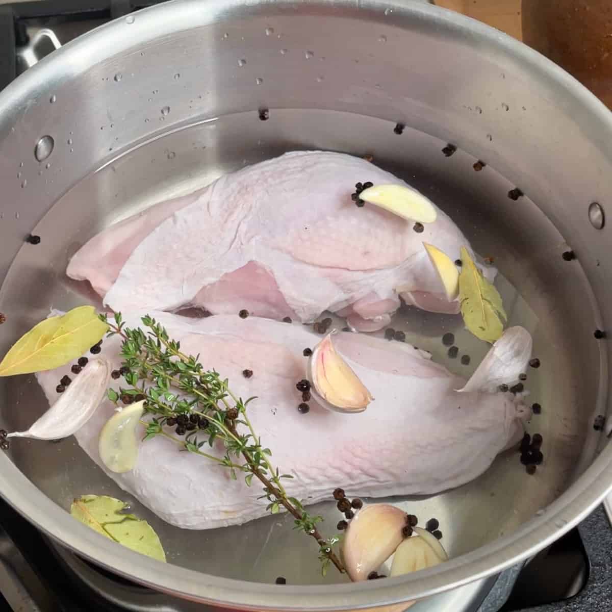 2 turkey breasts in brine inside a large stainless steel pot.