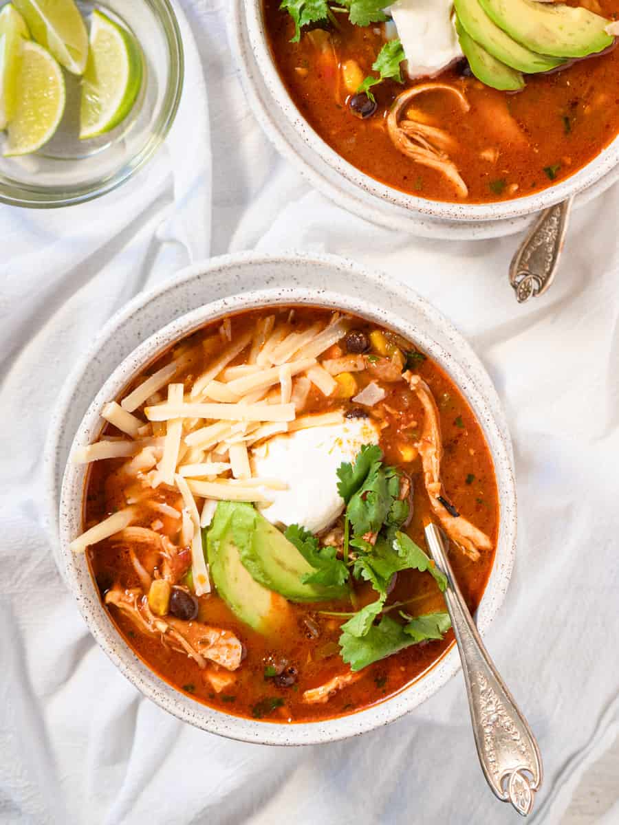 single bowl of enchilada soup topped with shredded cheese, avocado, sour cream, and fresh cilantro.