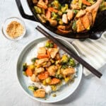 one serving of sesame chicken stir fry with chopsticks. Cast iron skillet on the side with the rest of the stir fry.