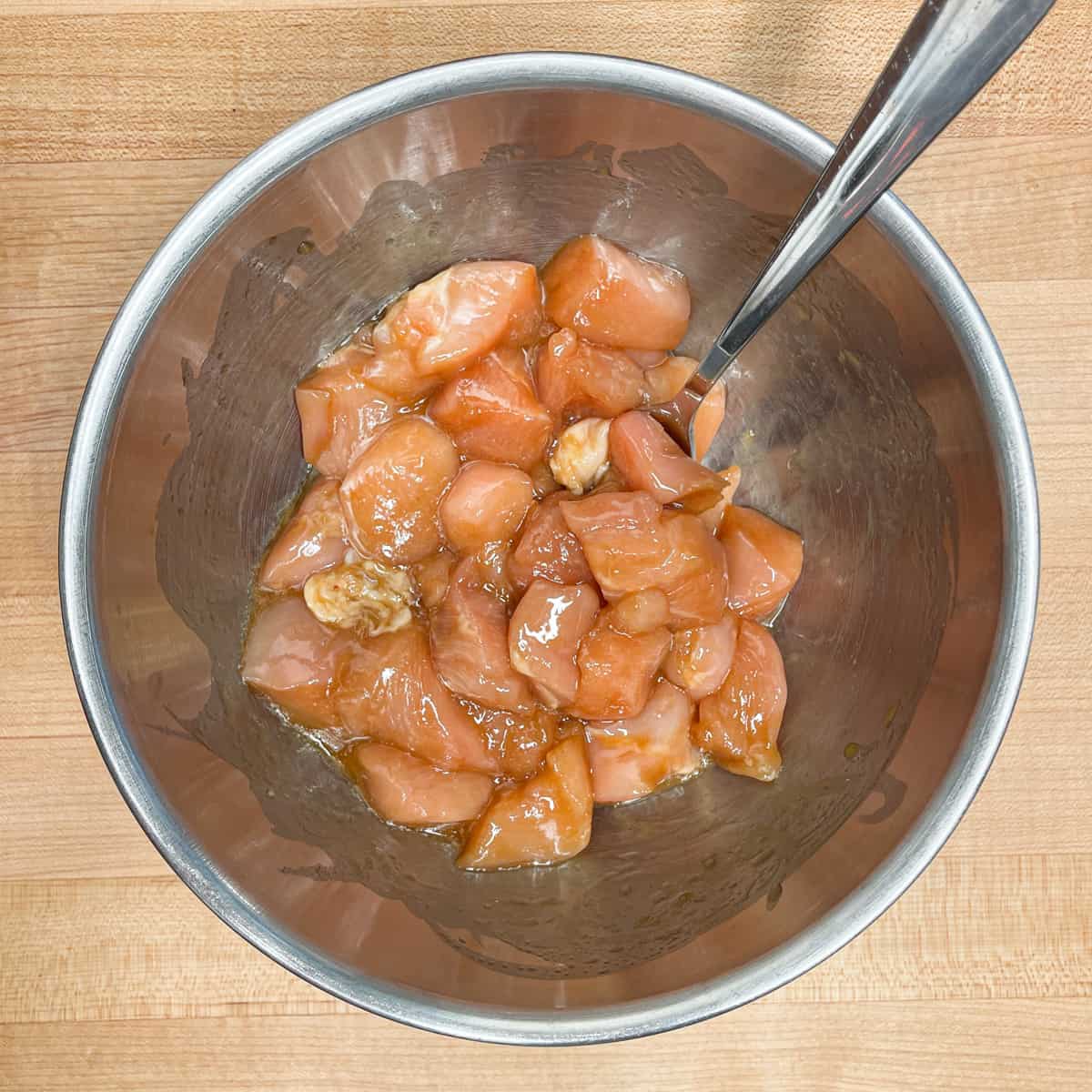 chicken pieces in a stainless steel bowl mixed with cornstarch and oil. 