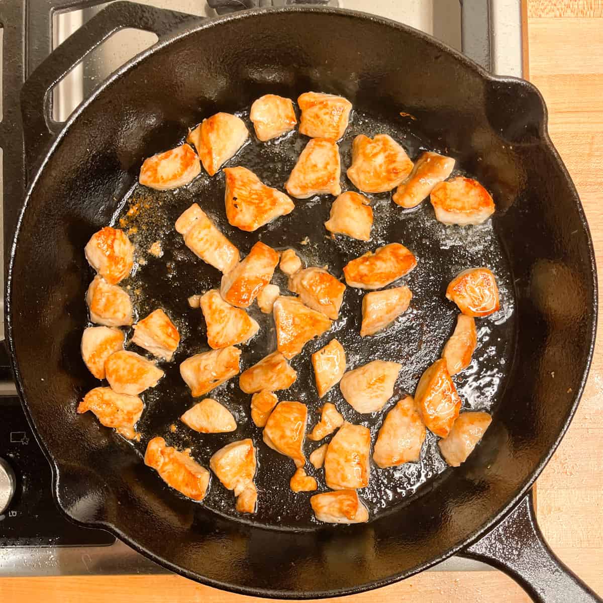 chicken pieces frying in a cast iron pan. 