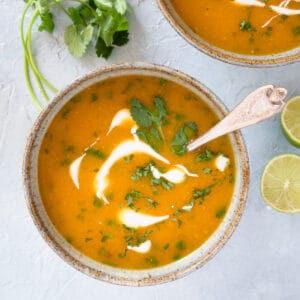 single serving of soup in a ceramic bowl with a spoon, garnished with coconut milk and fresh cilantro.
