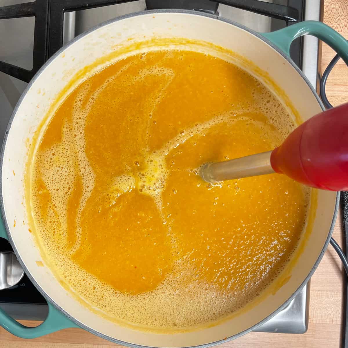 pot of soup with a hand blender being used to puree.