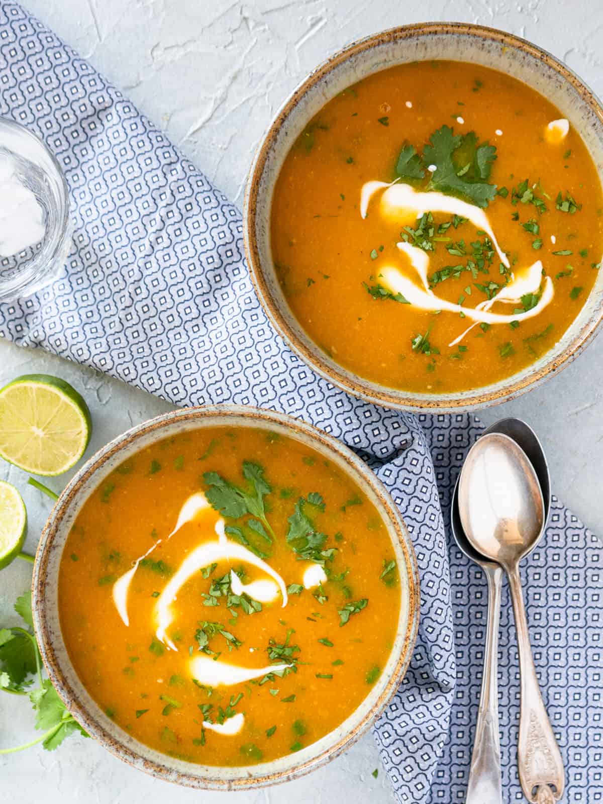 2 bowls of soup with 2 spoons and fresh limes on the side. Soup is garnished with sour cream and cilantro. 