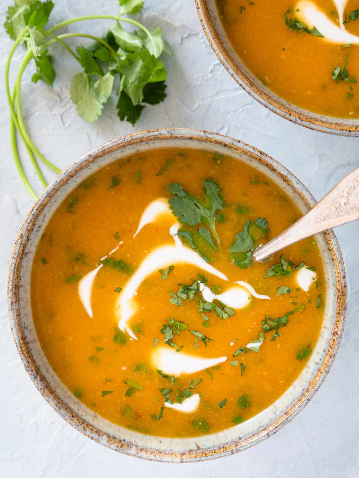 single serving of soup in a ceramic bowl garnished with coconut milk and fresh cilantro.