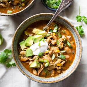 one bowl of chili with a spoon topped with avocado, sour cream and green onions.