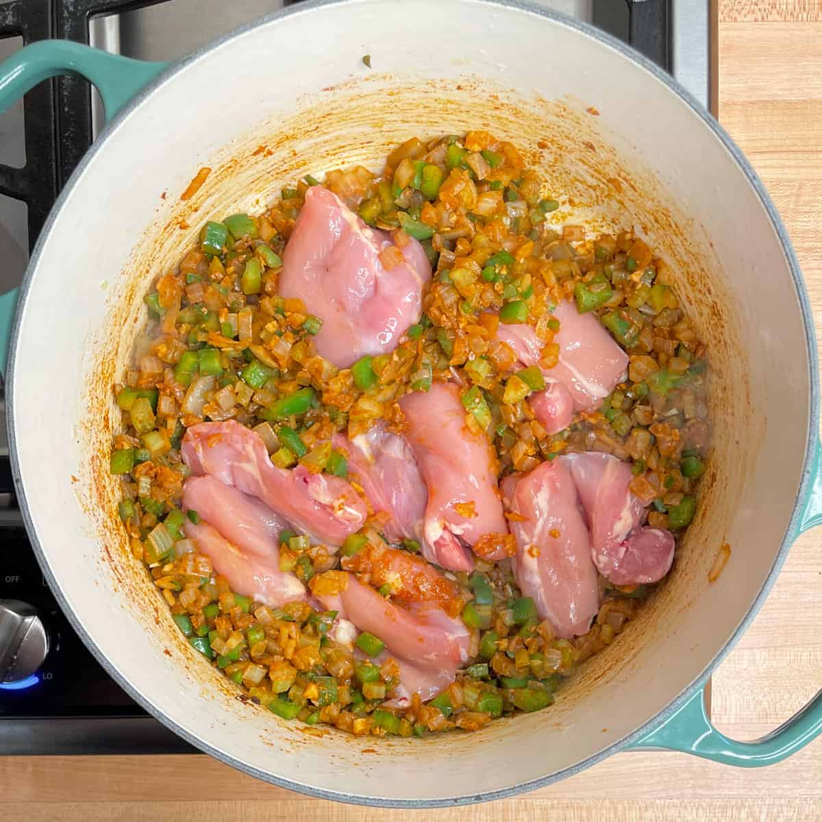 adding the chicken to the pot with the vegetables.