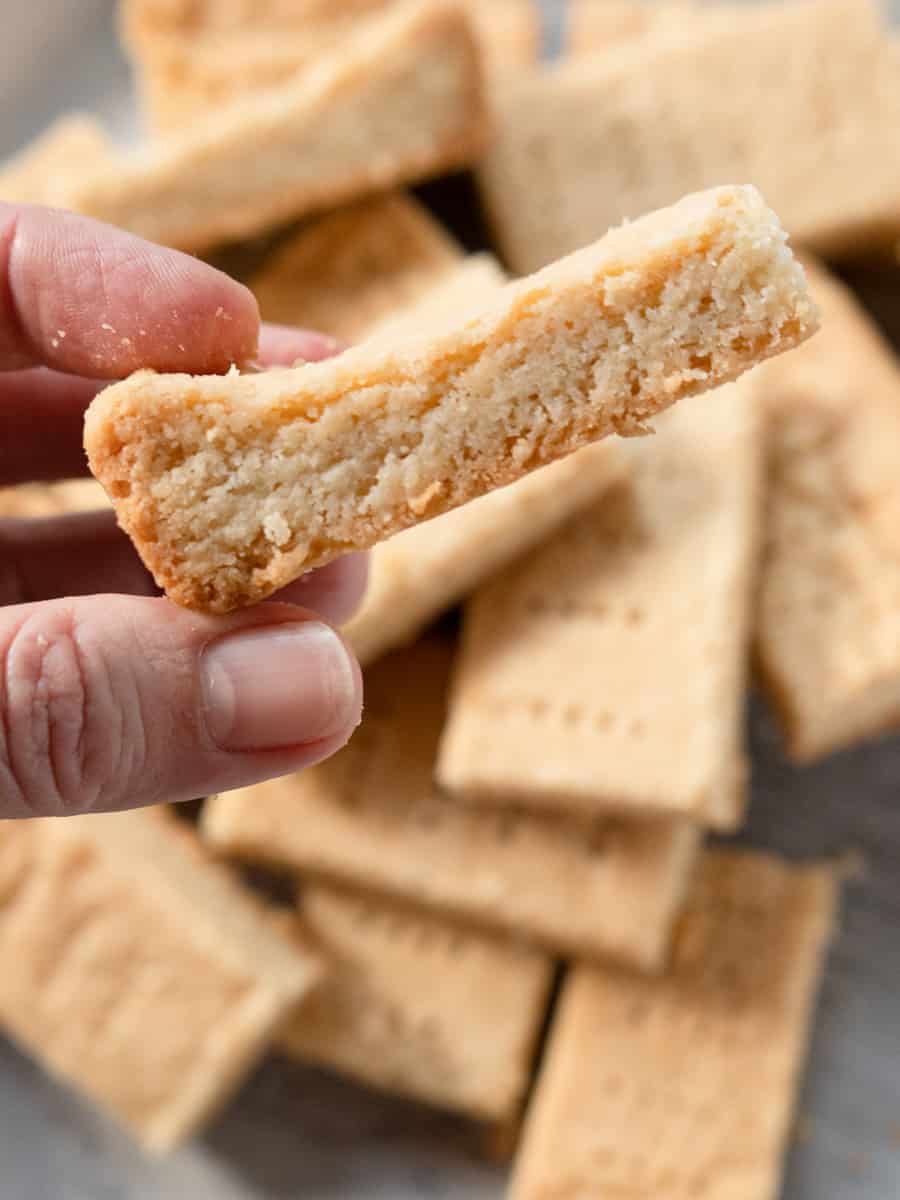 one piece of shortbread being held over a pile of cookies. 