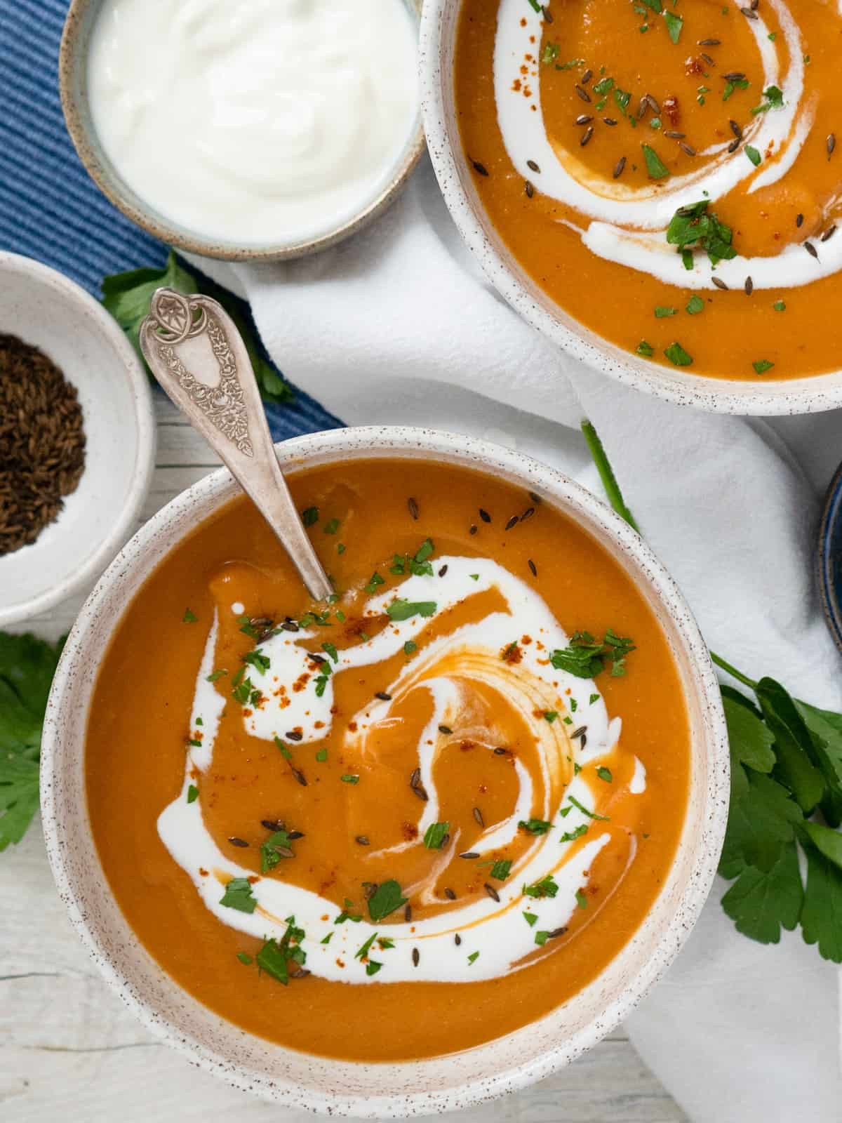 One bowl of soup with another off to the side. Small bowls of toasted cumin seeds and yogurt off to the side.