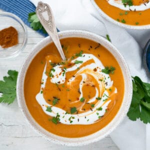 one bowl of carrot soup garnished with a swirl of yogurt, parsley and toasted cumin seeds.