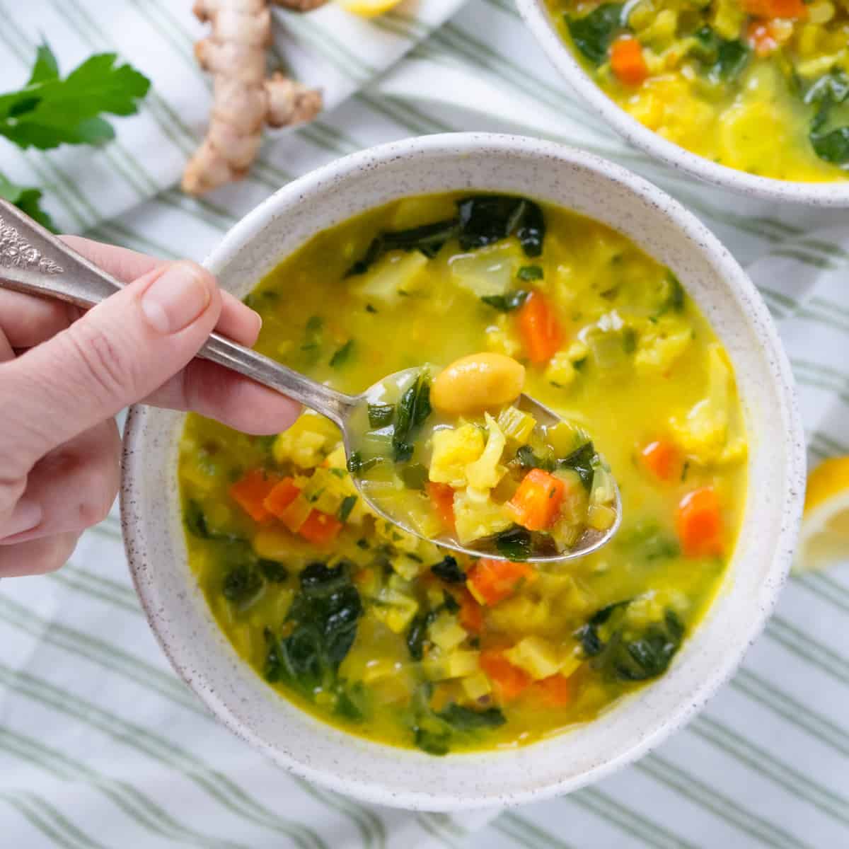 a partial hand holding a spoonful of soup over a bowl of soup.