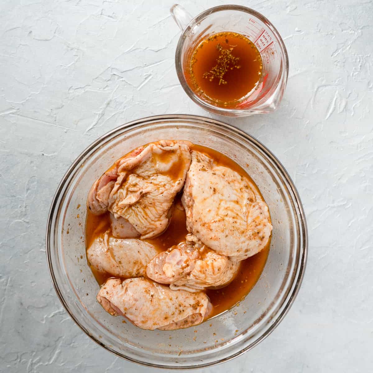 marinating chicken in a glass bowl with a measuring cup of marinade on the side.