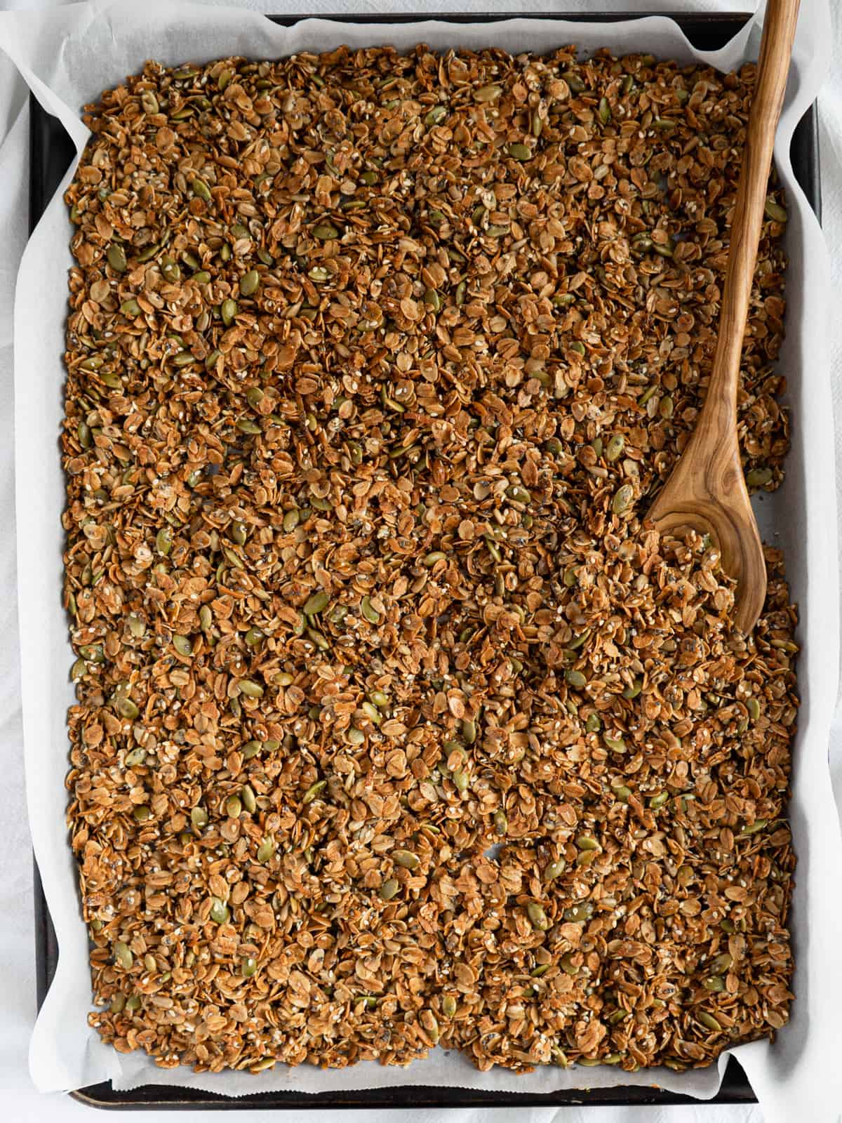 golden baked granola on a baking tray with a wooden spoon.