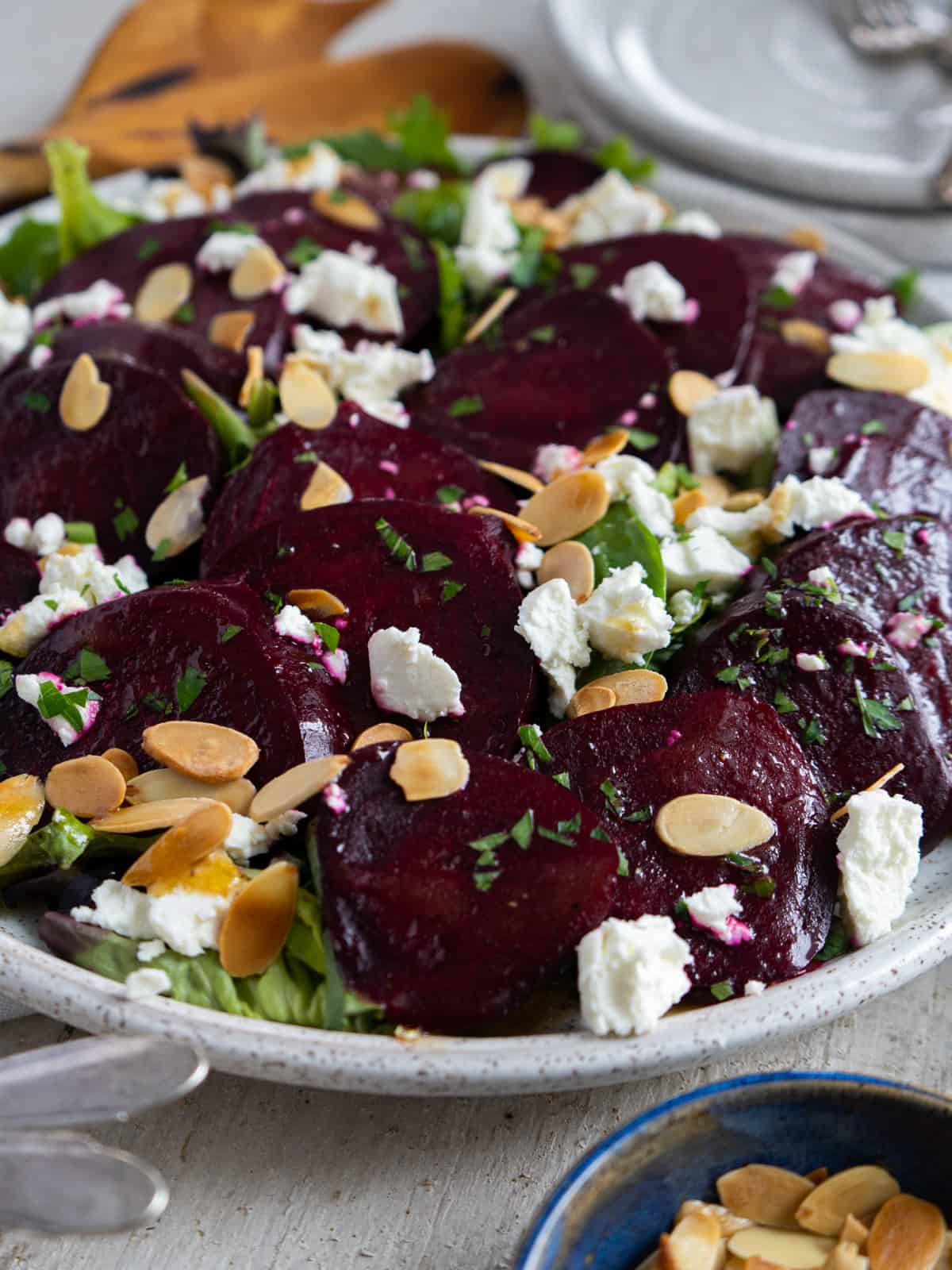 sliced beets on a platter on top of a bed of greens and topped with sliced almonds and crumbled goat cheese