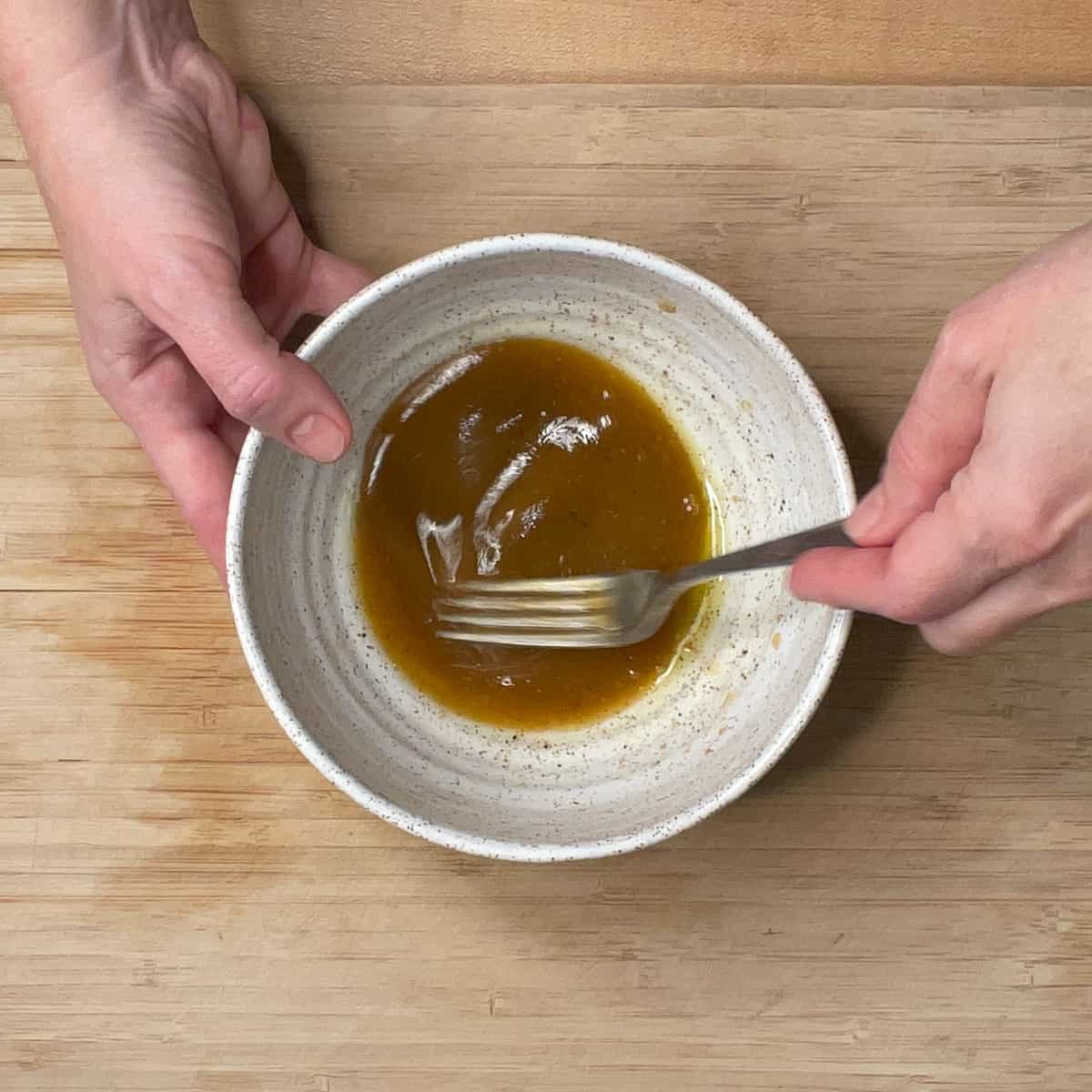Mixing together the salad dressing ingredients in a white ceramic bowl. 