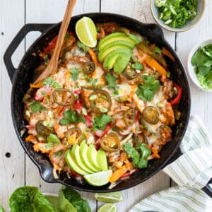 chicken fajita casserole in a cast iron skillet garnished with sliced avocado, cilantro and lime wedges.