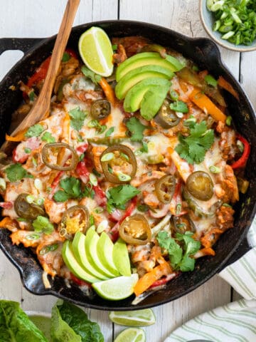 chicken fajita casserole in a cast iron skillet garnished with sliced avocado, cilantro and lime wedges.