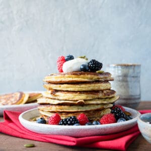 a stack of 6 pancakes topped with fresh berries and yogurt.