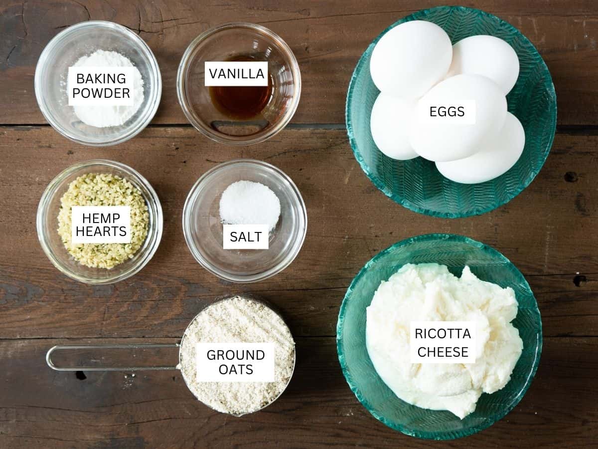 all ingredients to make ricotta pancakes labeled and on a dark wood background. 