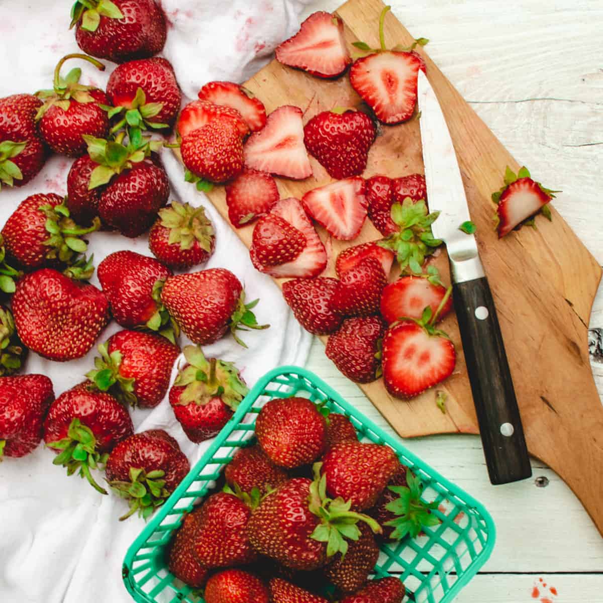 Sliced fresh strawberries on a wood board with a paring knife.