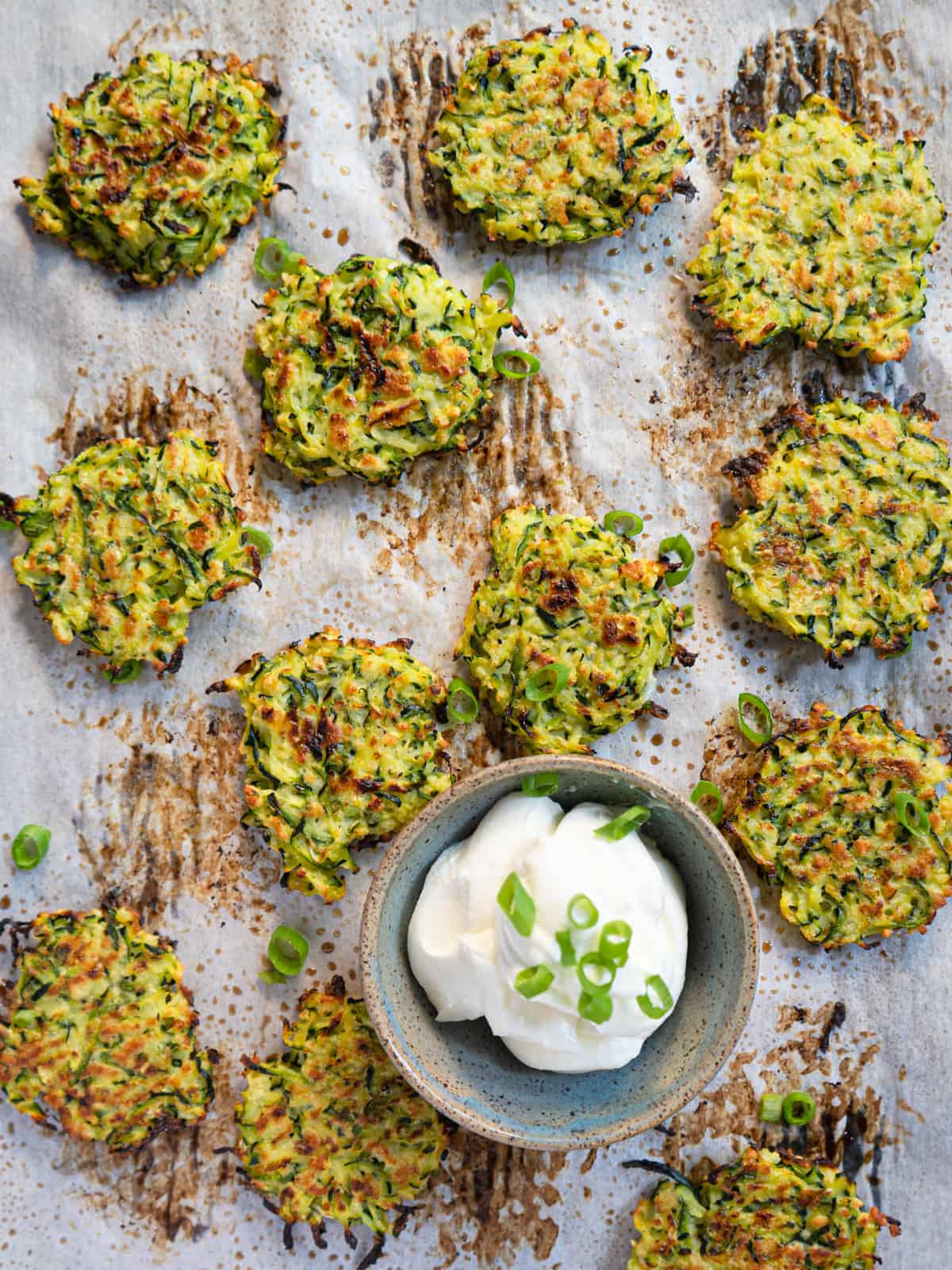 Baked zucchini fritters on a tray with a dish of sour cream garnished with green onions.