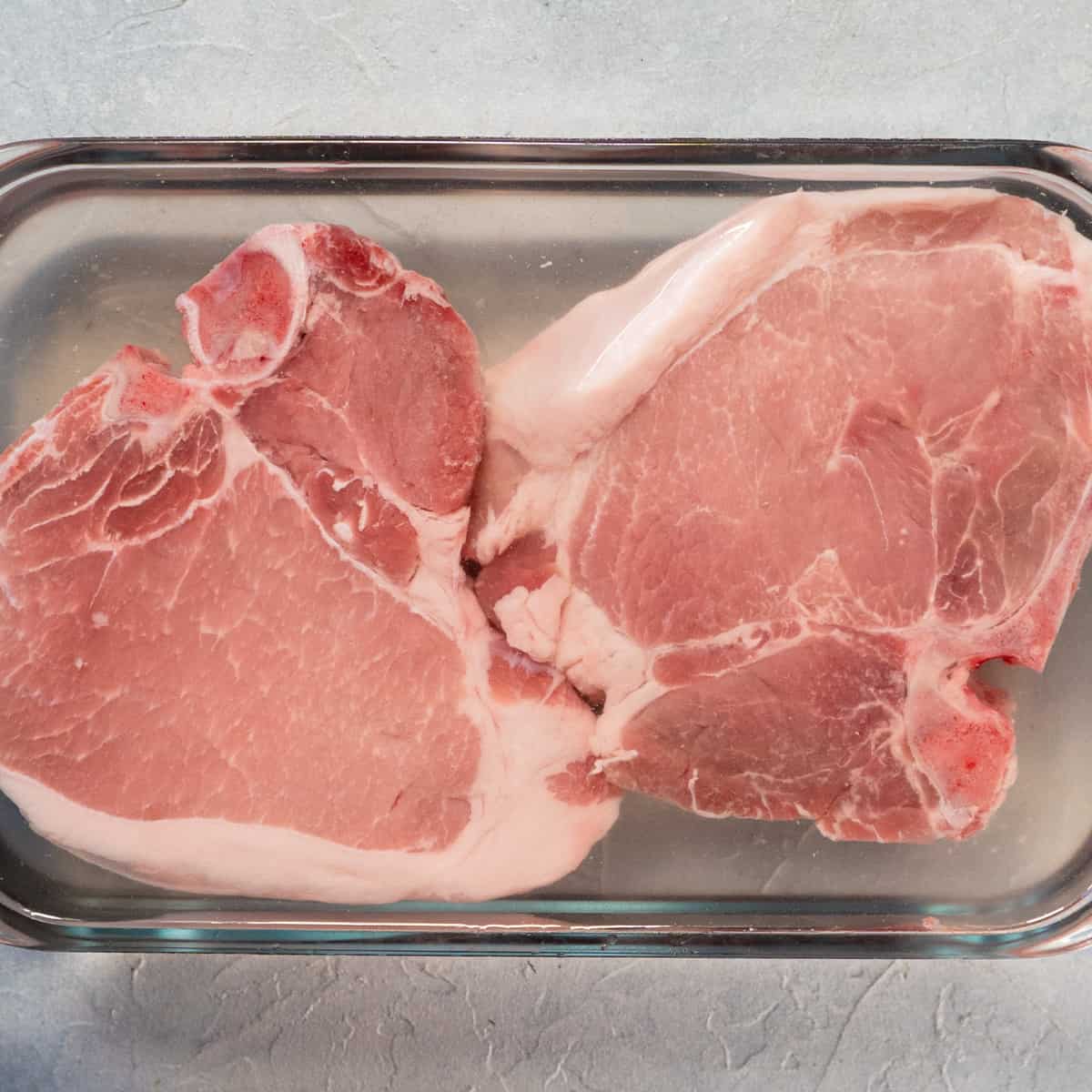 pork chops submerged in brining liquid in a glass dish.